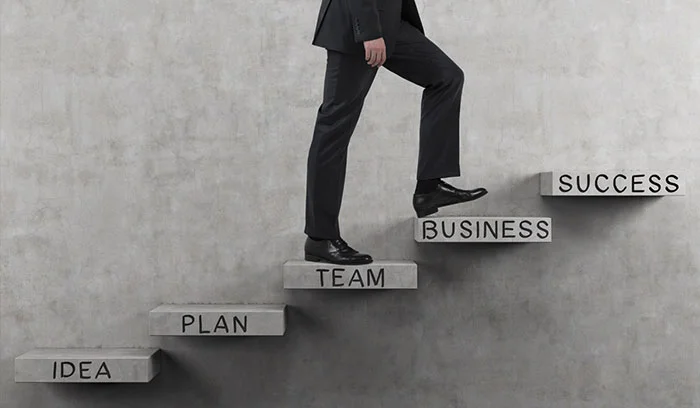 مرد در حال بالا رفتن از پله‌های IDEA، PLAN، TEAM تا SUCCESS