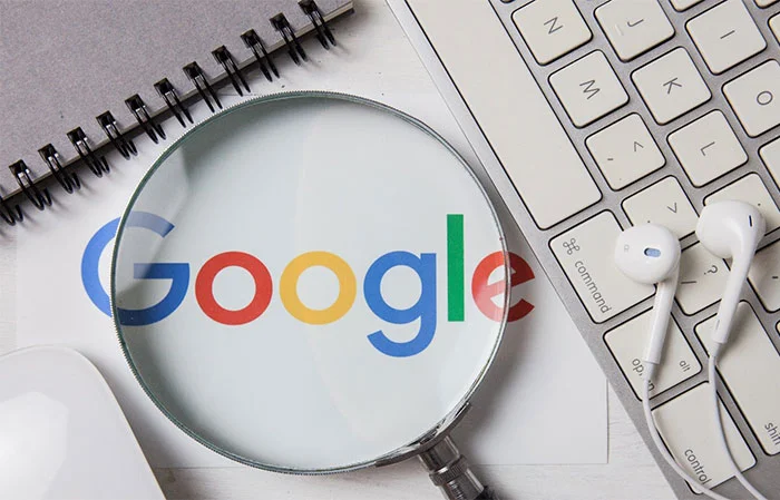 لوگوی Google زیر ذره‌بین روی میز کنار کیبورد و هندزفری سفید